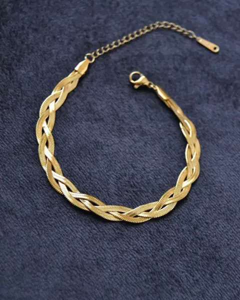 A braided gold bracelet on dark fabric